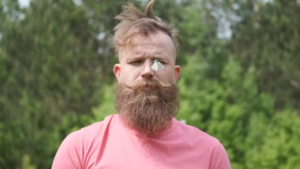 Man in het bos met vlinder, hipster in roze t-shirt, vlinder op zijn gezicht, grappig moment — Stockvideo