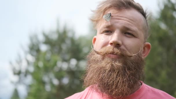 Mann mit Schmetterlingsinsekt im Gesicht, lustiger Moment, Hipster lächelnd, in rosa T-Shirt, — Stockvideo