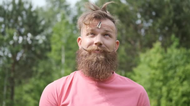 Man in het bos met vlinder, hipster in roze t-shirt, vlinder op zijn gezicht, grappig moment — Stockvideo