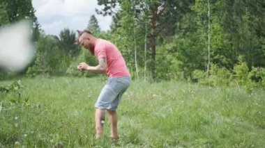 Adam çayırda kelebek yakalar, pembe tişört ve şortlu hipster, neşeli ruh hali.