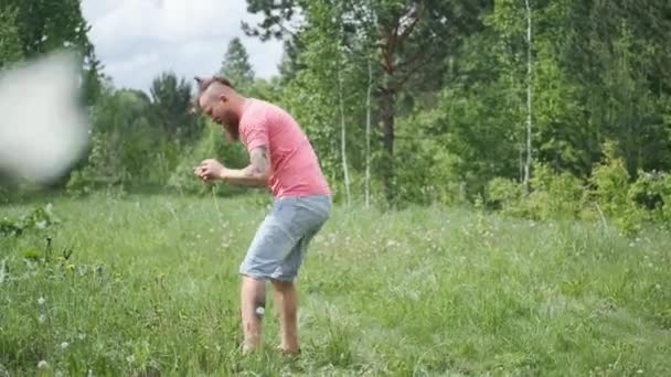 Mężczyzna łapie motyle na łące, hipster w różowej koszulce i szortach, dobry nastrój — Wideo stockowe