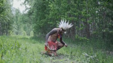 Kızılderili başlıklı bir adam elinde meşaleyle ateş yakıyor.