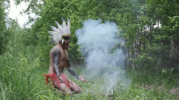 O homem na cobertura para a cabeça de índios americanos nativos acende fogo, em tempos primitivos — Vídeo de Stock