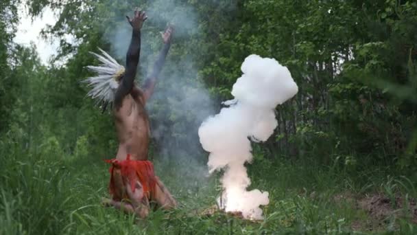 Людина в головному уборі корінних американських індіанців запалює вогонь у примітивні часи — стокове відео