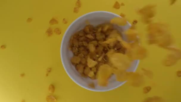 Los cereales de desayuno se vierten en un tazón blanco, aislado sobre un fondo amarillo — Vídeos de Stock