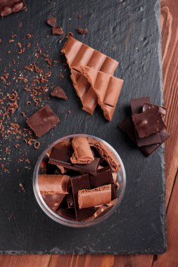 Karanlık ve sütlü çikolata bar ve siyah taş tahta parçaları. Tatlılar ve tatlılar bir kavram. Gıda arka plan üstten görünüm