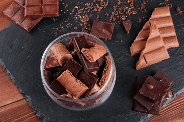 Karanlık ve sütlü çikolata bar ve siyah taş tahta parçaları. Tatlılar ve tatlılar bir kavram. Gıda arka plan üstten görünüm
