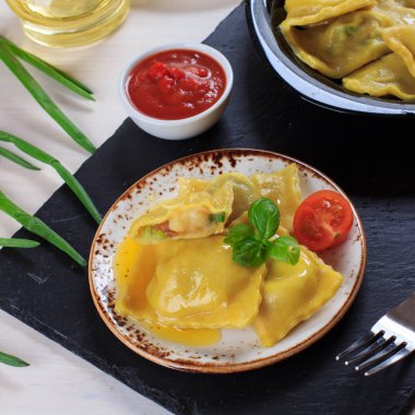 Geleneksel İtalyan ev yapımı ravioli makarna patates ve domates soslu ıspanak ile doldurulmuş, zeytinyağı ve fesleğen siyah bir taş tahta üzerinde
