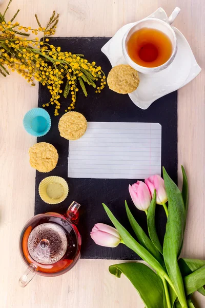 Kadınlar Günü tebrik kartı laleler, Mimoza, çay ve kek siyah taş tahta arka plan üzerinde.