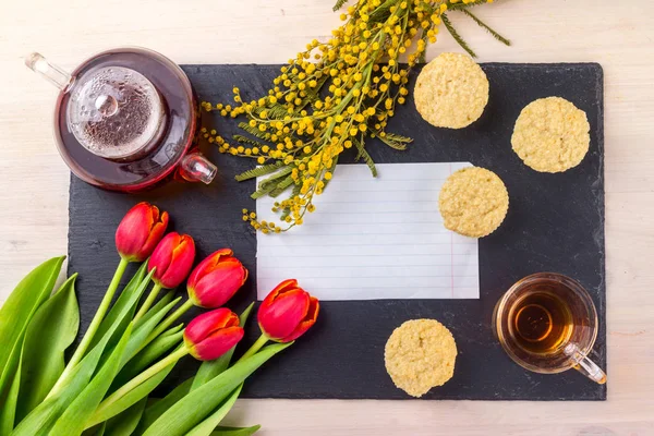 Kadınlar Günü tebrik kartı laleler, Mimoza, çay ve kek siyah taş tahta arka plan üzerinde.