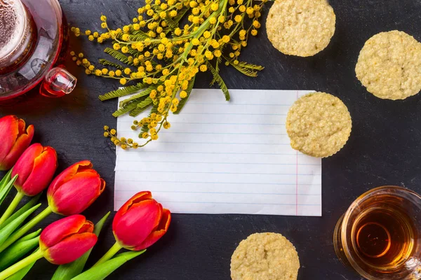 Kadınlar Günü tebrik kartı laleler, Mimoza, çay ve kek siyah taş tahta arka plan üzerinde.