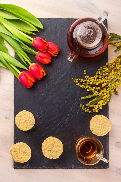 Kadınlar Günü tebrik kartı laleler, Mimoza, çay ve kek siyah taş tahta arka plan üzerinde.