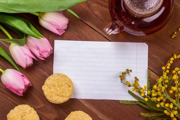 Kadınlar Günü tebrik kartı laleler, Mimoza, çay ve kek kahverengi ahşap zemin üzerinde.