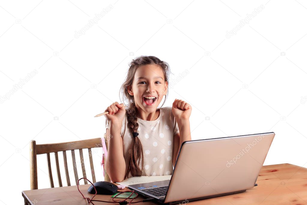 A 10 years old school girl sitting at a table with a laptop with an expressive emotional face isolated on white. Successful pass of exam, good scores for test, online education, homeschooling concept
