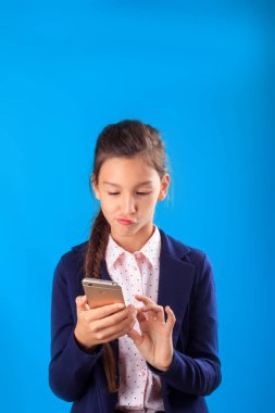 Sevimli okul kız öğrenci pensive yüzü ile ekrana bakarak smarthphone tutarak ve metin yazarak. Gençlik bloglama, yorum, internet kavramı yazma