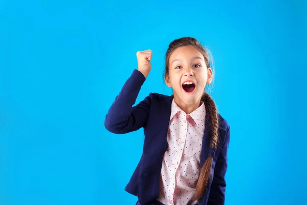 Angry shouting aggressive school girl expressing negative emotions shaking her fist on blue background with copy space. Stress and bullying at school concept