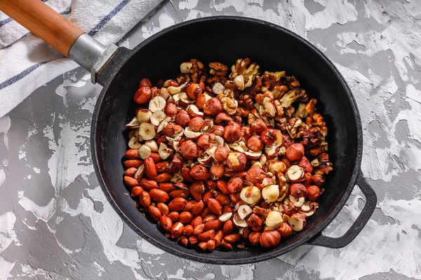 Roasted nuts in a cast iron pan on a concrete background. Ingredients for making muesli or granola.