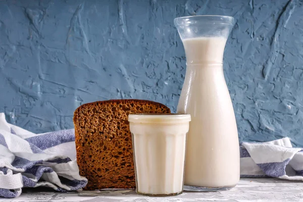 Fresh milk in a glass bottle and in a glass with black bread on a concrete background.