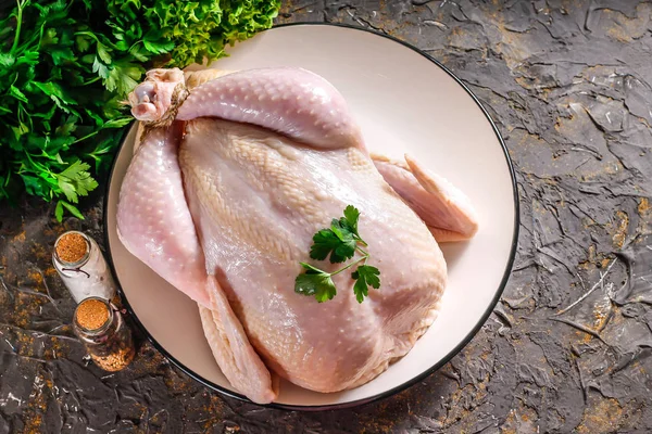 Fresh chicken for baking on a dish, spices with herbs and stone. Raw chicken is an ingredient for making food. Chicken for baking on Independence Day.