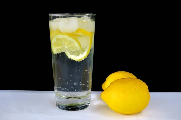 黒い背景に透明なガラスにレモンと輝く水 — ストック写真