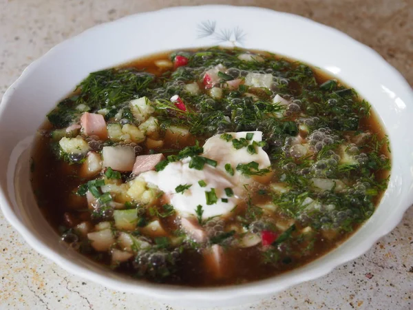 Traditional Russian cold soup with kvass to eat in hot weather. Healthy vegetable soup in a white plate  is on the table.