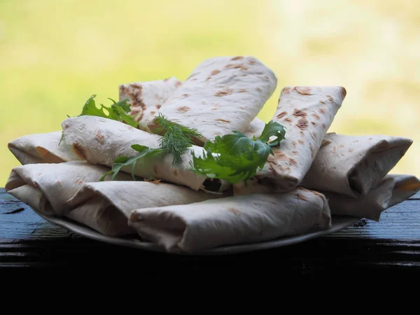 Fried bread rolls lavash filled with herbs and cheese in a white plate on a dark table.