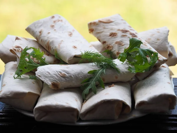 Fried bread rolls lavash filled with herbs and cheese in a white plate on a dark table.