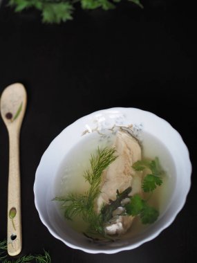 Olympus Dijital Fotoğraf Makinesi Beyaz bir tabakta tavuk ve otlar ve koyu bir masada bir kaşık ile Şeffaf et suyu. Dikey resim. 