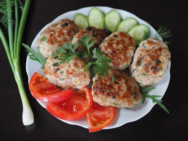 Protein meat dish with a golden crust to cook with herbs and vegetables for the diet. Chopped steak with vegetables and herbs are in a white plate on a dark table.