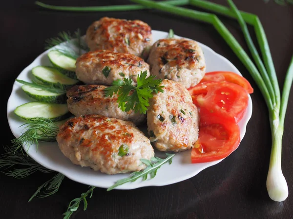 Protein meat dish with a golden crust to cook with herbs and vegetables for the diet. Chopped steak with vegetables and herbs are in a white plate on a dark table.