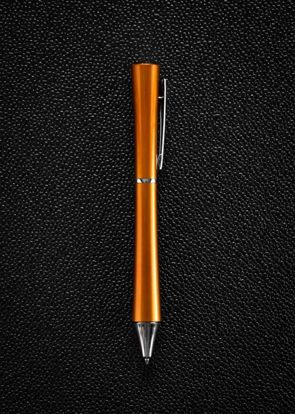 Orange ballpoint pen on dark background.