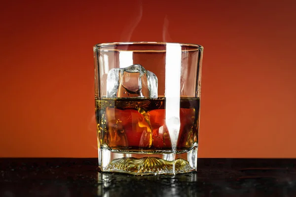 Glass of whiskey and ice cube on red background and cooling smoke. Close Up of whisky glass with alcohol drink.