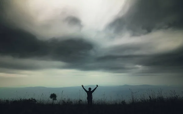 Silhouette of alone man standing in the tall grass on the mountain view with cloudy sky in nature background. Backpacker travel lifestyle and happy concept.