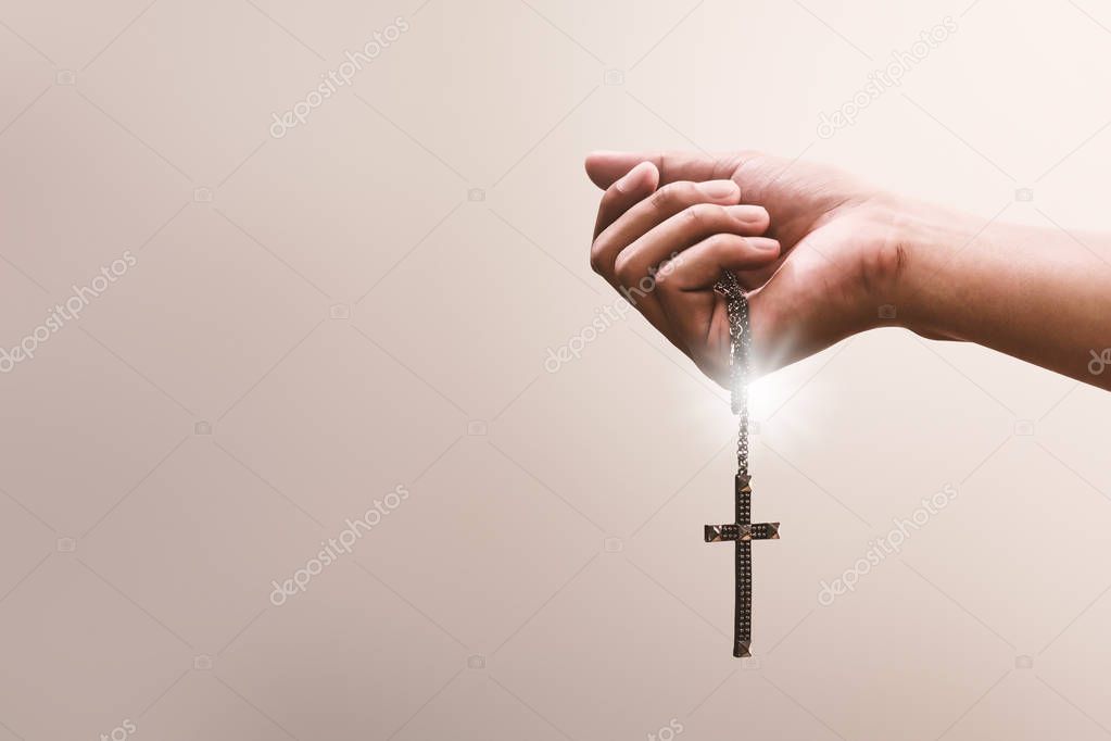 Praying hands hold a crucifix or cross of metal necklace with faith in religion and belief in God on confession background. Power of hope or love and devotion.