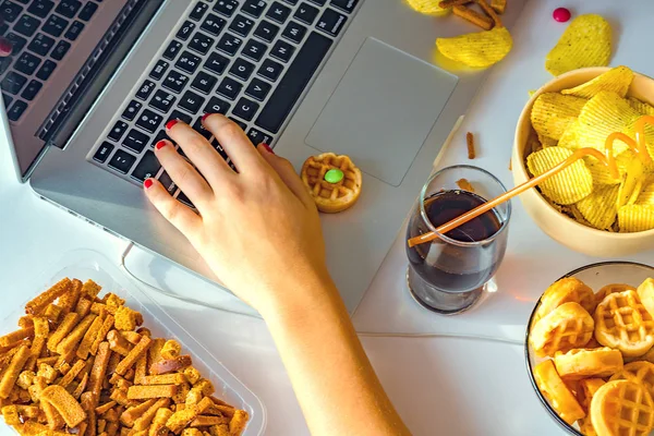 Kız bilgisayar başında çalışıyor ve fast food yiyor. Sağlıksız yiyecekler: cips, kraker, şeker, waffle, kola. Abur cubur, konsept.