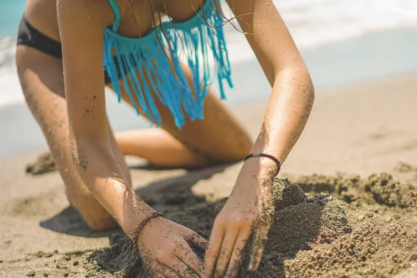 Mooi meisje in bikini bouwt een zandkasteel op het strand — Stockfoto