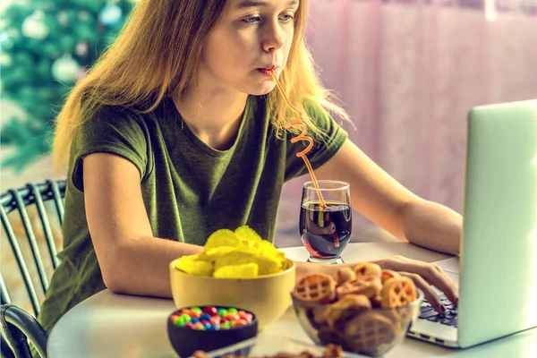 Kız bilgisayar başında çalışıyor ve fast food yiyor. Sağlıksız yiyecekler: cips, kraker, şeker, waffle, kola. Abur cubur, konsept.