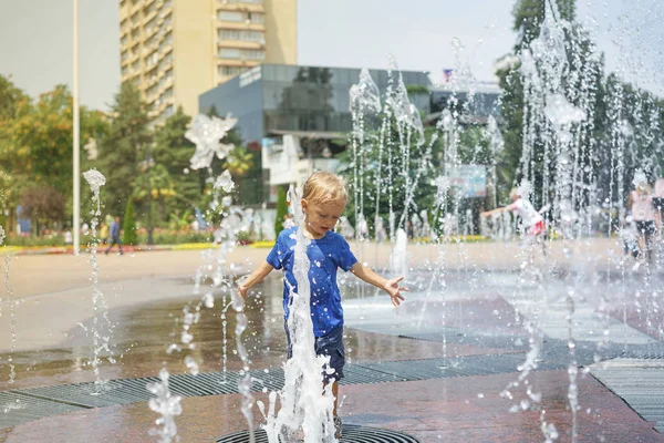 A boy playing with water in park fountain. Hot summer. Happy young boy has fun playing in water fountains