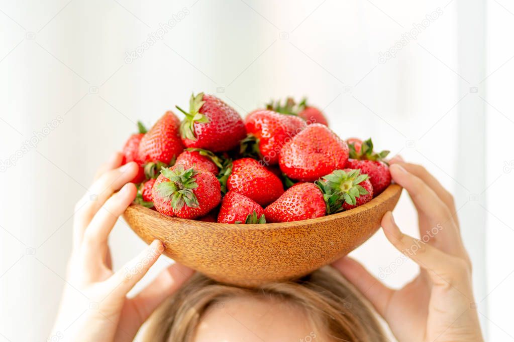 Wooden plate with strawberries in girl hand on light background, organic food concept