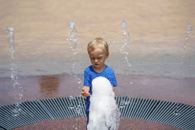 Park çeşmesinde suyla oynayan bir çocuk. Sıcak yaz. Mutlu genç çocuk su çeşmeleri oynarken eğleniyor 