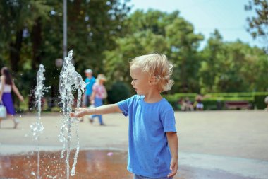 Park çeşmesinde suyla oynayan bir çocuk. Sıcak yaz. Mutlu genç çocuk su çeşmeleri oynarken eğleniyor 