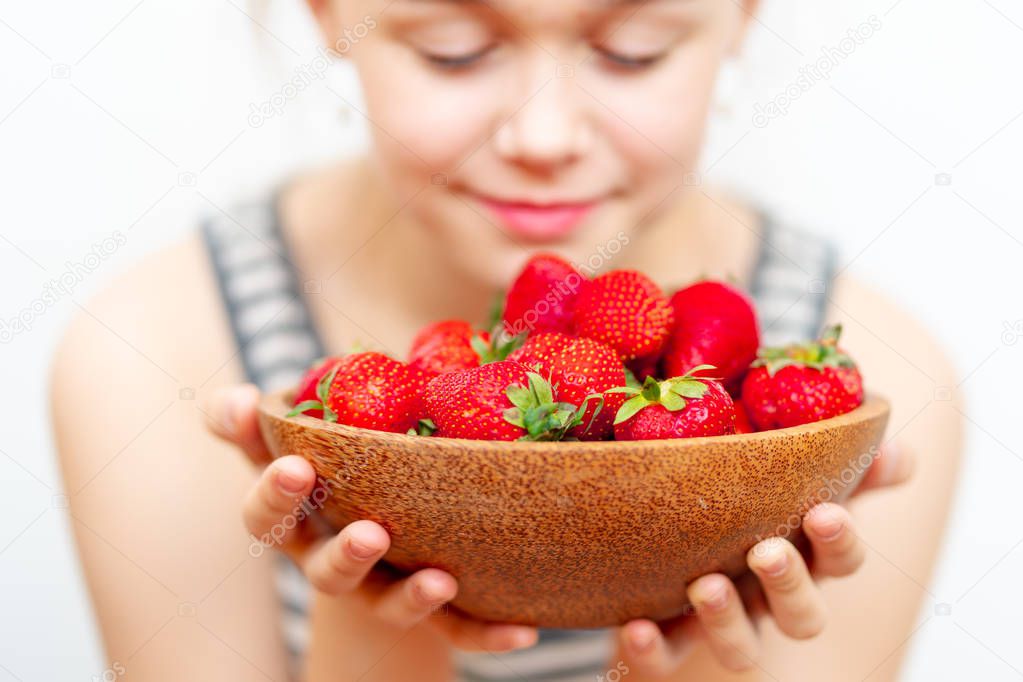 Wooden plate with strawberries in girl hand on light background, organic food concept