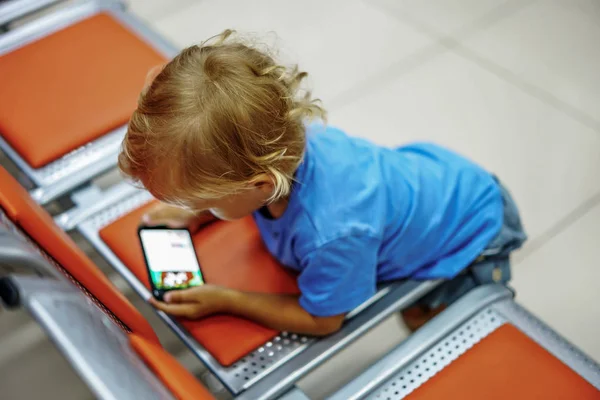 Cute little boy watching cartoons on smartphone in empty waiting
