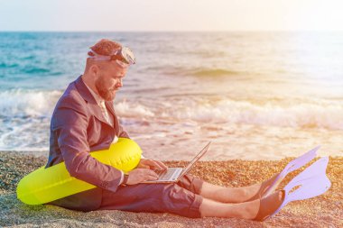 Başarılı işadamı şnorkelli yüzme araçları giyen dizüstü bilgisayar ile sahilde çalışıyor
