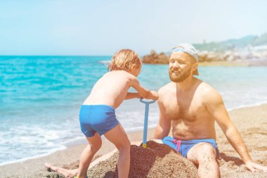 Mutlu baba ve oğul tropik sahilde kumda birlikte oynuyor