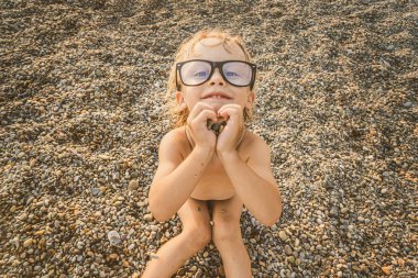 Çakıl üzerinde güneşlenen büyük gözlük sevimli komik küçük çocuk olmak