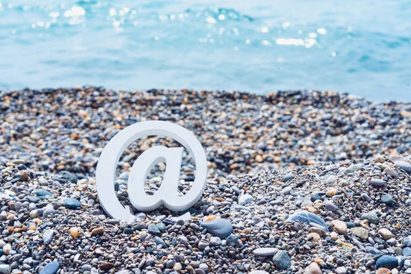 Deniz arka planda deniz çakıl üzerinde e-posta işareti. — Stok fotoğraf