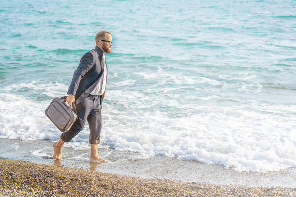 Happy businessman walking along the seashore. Vacations Concept