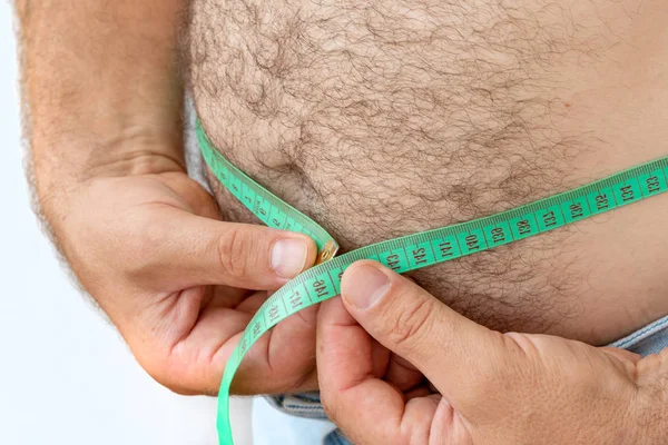 A man measures his fat belly with a measuring tape.