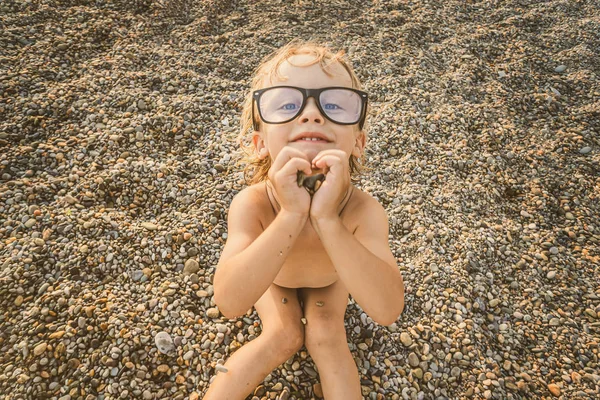 Çakıl üzerinde güneşlenen büyük gözlük sevimli komik küçük çocuk olmak